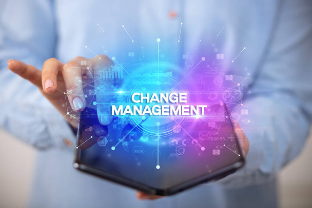 Businessman holding a foldable smartphone with CHANGE MANAGEMENT inscription, new business concept - 写真・画像