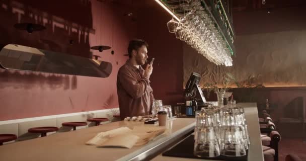 Valós idejű kézi lövés a fiatal férfi borozó tulajdonosa beszél mobiltelefonon ügyfél foglalási asztal estére, miközben áll a pultnál - Felvétel, videó