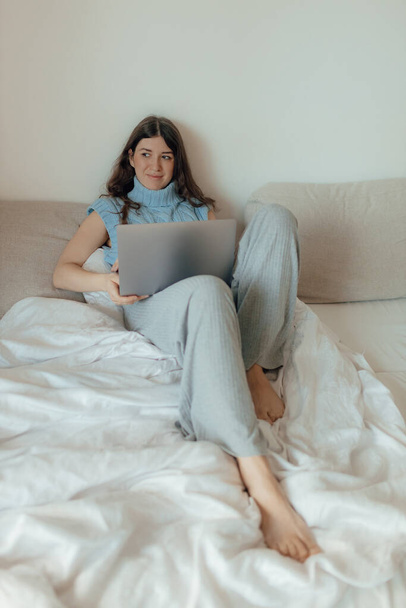 若い女性は、ベッドルームでは、新鮮な輝きを構成するポーズ、ノートパソコンの自宅の書き込みメッセージに座っている。ソフトフォーカスとノイズと写真のコンセプト。テクノロジーとコンテンツマーケティングのコンセプト. - 写真・画像