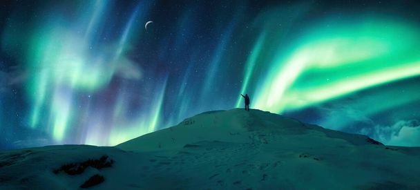 Güzel Aurora Borealis, Kuzey ışıkları gölgelerin üzerinde parlıyor Arktik dairesindeki gece gökyüzünün tepesinde duran yürüyüşçü. - Fotoğraf, Görsel