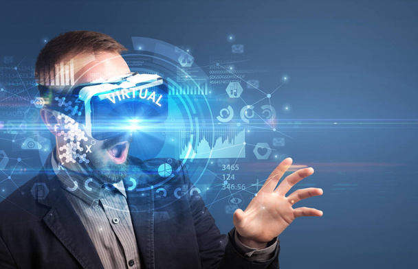 Businessman looking through Virtual Reality glasses with VIRTUAL inscription, innovative technology concept - Photo, Image