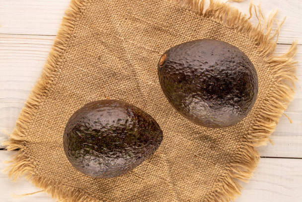Two ripe avocados with a jute napkin on a wooden table, macro, top view. - Photo, Image