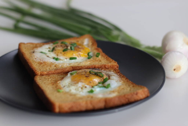 Bulls eye on bread toast. Egg fried in a hole made in the centre of toast. A quick breakfast option, also called bulls eye toast or egg in the basket or egg in a hole. Shot along with spring onions. - Photo, Image