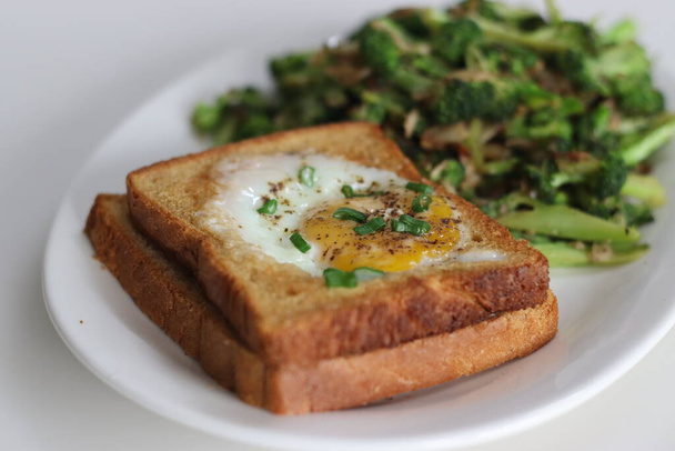 Bulls oog op brood toast. Eieren gebakken in een gat gemaakt in het midden van toast geserveerd met roergebakken broccoli. Een snelle ontbijt optie, ook wel stieren oog toast of ei in de mand of ei in een gat - Foto, afbeelding