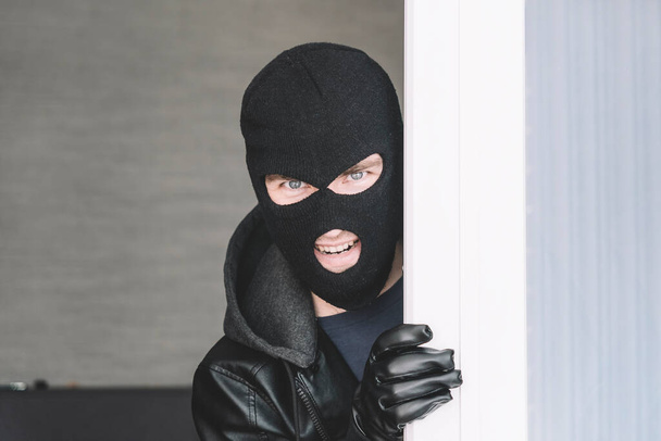 Kradziony przestępca w czarnej kominiarce zakradający się do domu przez okno lub szklane drzwi. przestrzeń kopiowania - Zdjęcie, obraz