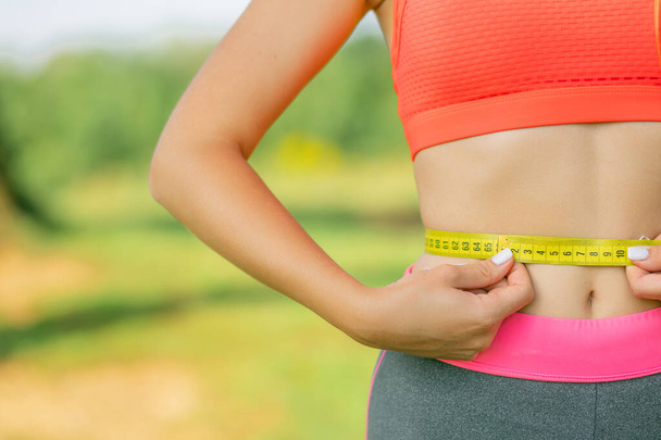 Young woman holding measuring tape on her thin waist. Unrecognizable slim lady in crop top showing her weightloss achievement after home workouts. Copy space - Zdjęcie, obraz
