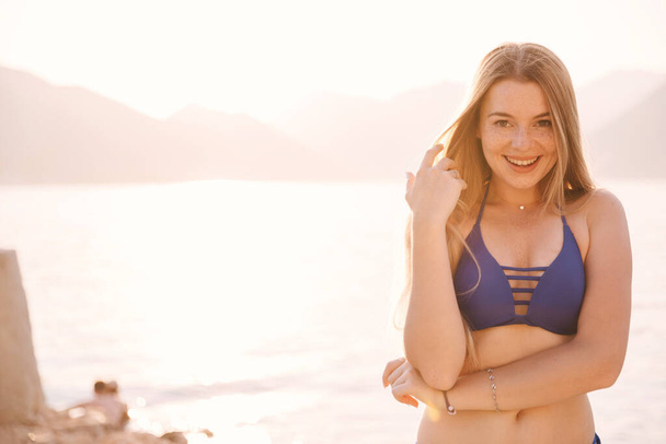 Sahilde durup kameraya bakan çekici bir kadının portresi. Mutlu gülümseyen kız yaz tatilinde deniz kenarında dinleniyor. Boşluğu kopyala - Fotoğraf, Görsel