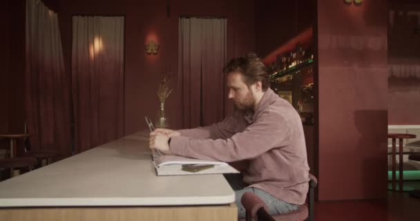 Side view kézi lövés szakállas férfi vállalkozó ül a pultnál belépő információkat adók dokumentumok a netbook, miközben a számlákat a bárban - Felvétel, videó