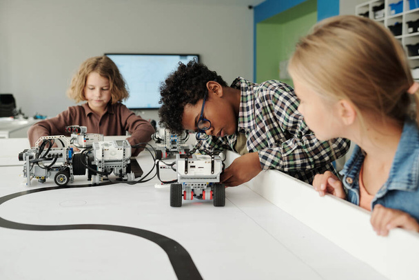 おもちゃの動きをコントロールしながら、テーブルごとにロボットの新しいモデルで遊ぶかわいい異文化間の子供たちのグループ - 写真・画像