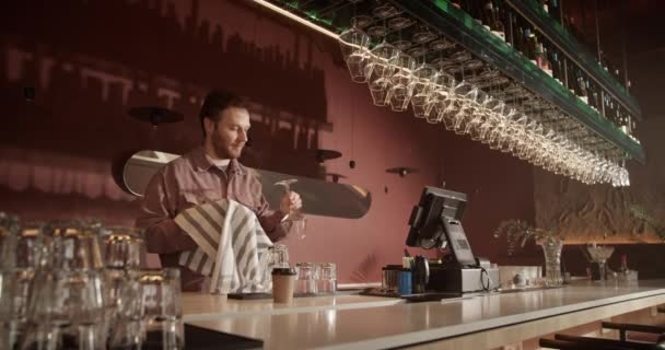 Портативный снимок молодого предпринимателя с низким углом перемещения стаканов на стойке из-под стебля в современном баре, готовясь к открытию уборки - Кадры, видео