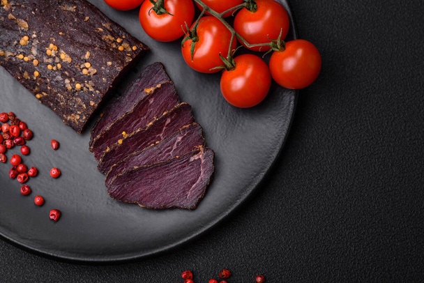 Delicious smoked Armenian basturma with spices and herbs sliced on a dark concrete background - Photo, Image