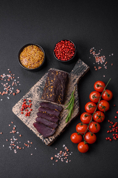 Delicious smoked Armenian basturma with spices and herbs sliced on a dark concrete background - Photo, Image