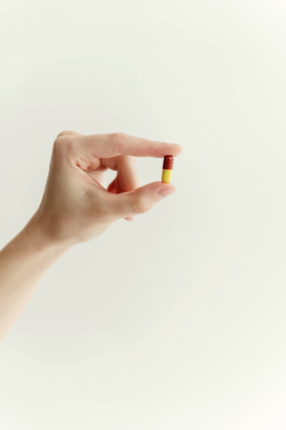 close-up of a hand holding a pill in the fingers on an isolated white background. one tablet red-yellow shell. medicine - Fotó, kép