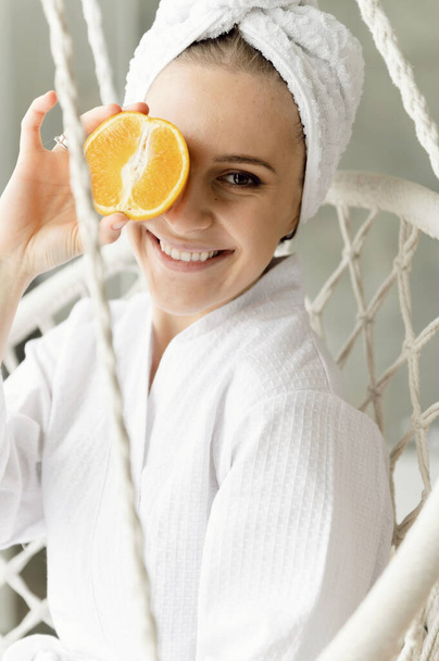 portrait of a cute girl who covers her joyful face with a cut orange. healthy lifestyle concept. body care. medium plan. - Фото, изображение