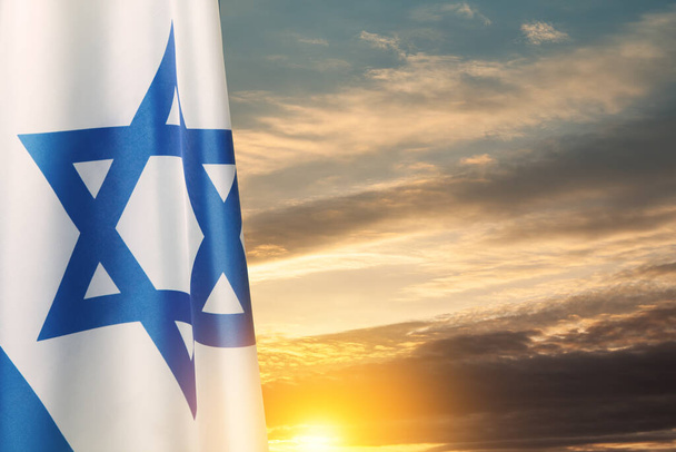 Israel flag with a star of David over cloudy sky background on sunset. Patriotic concept about Israel with national state symbols. Banner with place for text. - Zdjęcie, obraz