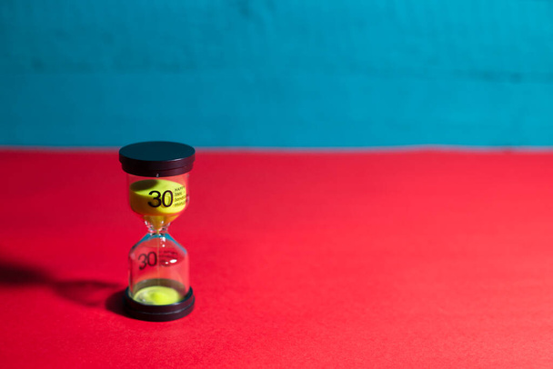 an hourglass with green sand on a blue-red background - Photo, Image