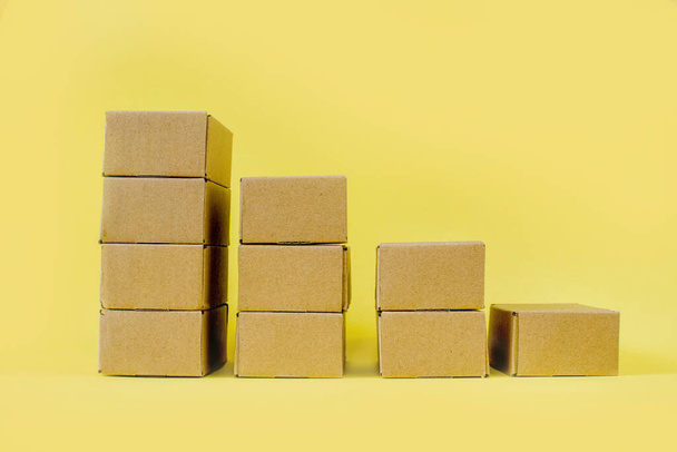 Closed kraft cardboard boxes are stacked in a descending row on a yellow background. Concept of delivery and storage of goods. - Foto, Imagem