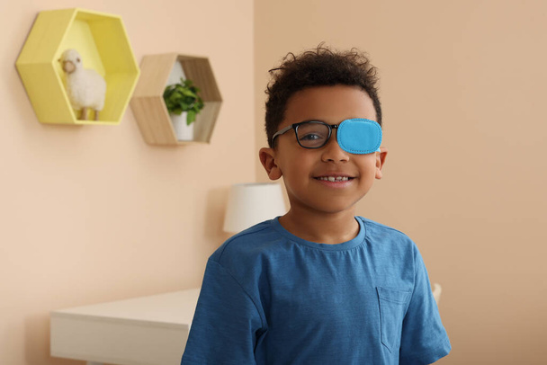 African American boy with eye patch on glasses in room, space for text. Strabismus treatment - 写真・画像