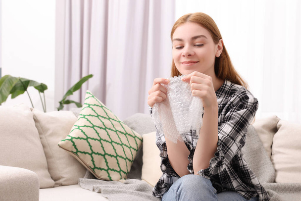 Woman popping bubble wrap on sofa at home, space for text. Stress relief - 写真・画像