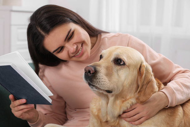 Happy woman sitting with cute Labrador Retriever on sofa at home - Photo, image