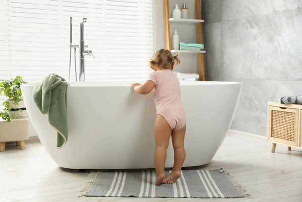 Симпатична маленька дівчинка біля ванни у ванній, вид ззаду
 - Фото, зображення