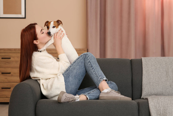 Woman kissing cute Jack Russell Terrier dog on sofa at home. Space for text - Fotó, kép