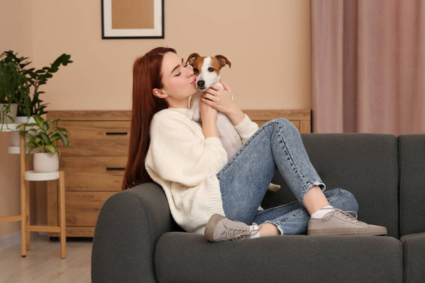 Woman kissing cute Jack Russell Terrier dog on sofa at home - Foto, afbeelding