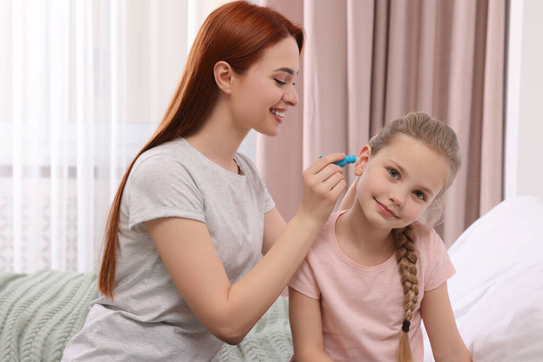 Mother dripping medication into daughter's ear in bedroom - Photo, image