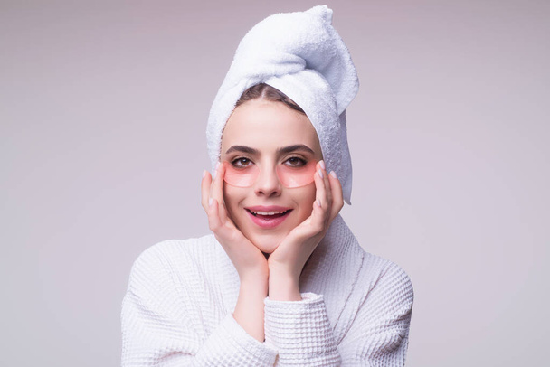 Eye patches, Beautiful girl with towel use facial eye patch. Beauty face. Young woman using eye patches, reduce puffiness and dark circles. Girl apply eye pads with hyaluronic acid for hydration - 写真・画像