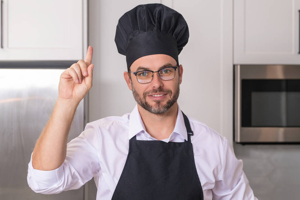 Idea for food. Portrait of happy chef man in a chef cap in the kitchen. Man wearing apron and chefs uniform and chefs hat. Character kitchener, chef for advertising - Photo, image