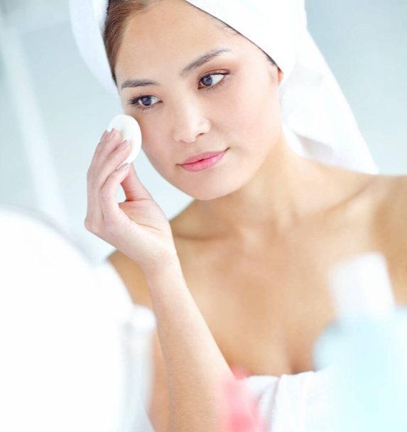 Keeping those wrinkles at bay...An attactive young Asian woman applying moisturizer with a towel on her head - Foto, Imagem