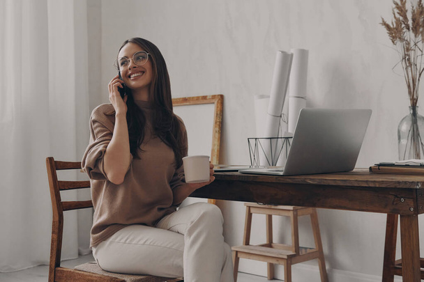 Happy woman talking on mobile phone while sitting at her workplace in home office - Photo, image