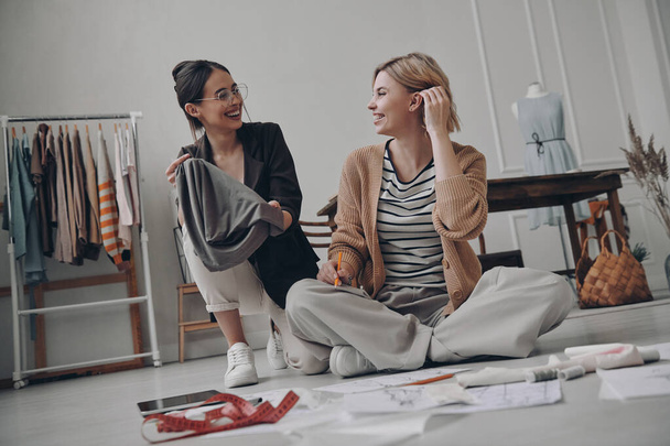 Two happy female fashion designers choosing textile while working in workshop together - Φωτογραφία, εικόνα