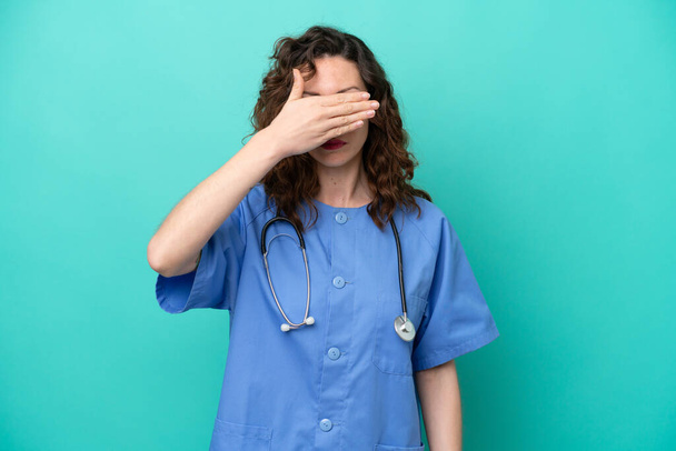 Jonge verpleegster Kaukasische vrouw geïsoleerd op blauwe achtergrond bedekt ogen door handen. Ik wil niets zien. - Foto, afbeelding