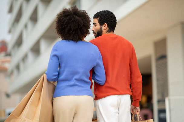 Shopping Offer. Rear View Of Shopaholics Couple Carrying Paper Shopper Bags And Packages Walking Back To Camera Near Modern Mall Outdoor. Weekend Sale Advertisement. Selective Focus - Fotoğraf, Görsel