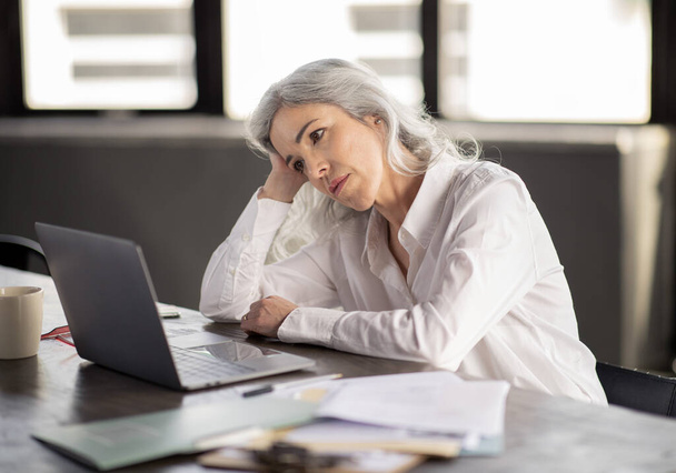 Stresowana biznesmenka siedząca przy biurku, korzystająca z laptopa, krzywiąca głowa na rękę, patrząca na ekran komputera w biurze. Nieszczęśliwa bizneswoman w miejscu pracy o wypalenie i cierpiących problemów z pracą - Zdjęcie, obraz