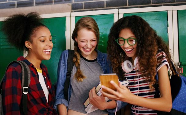 Tu dois venir voir ça. un groupe de jeunes écoliers naviguant ensemble sur un téléphone portable en attendant d'aller en classe à l'intérieur d'une école - Photo, image