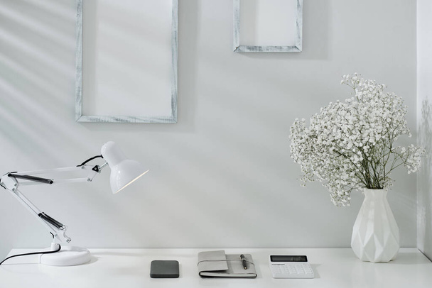 Planner, smartphone and calculator under lamp on white office desk - Foto, imagen