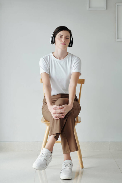 Młoda kobieta siedzi na krześle i słucha muzyki w słuchawkach - Zdjęcie, obraz