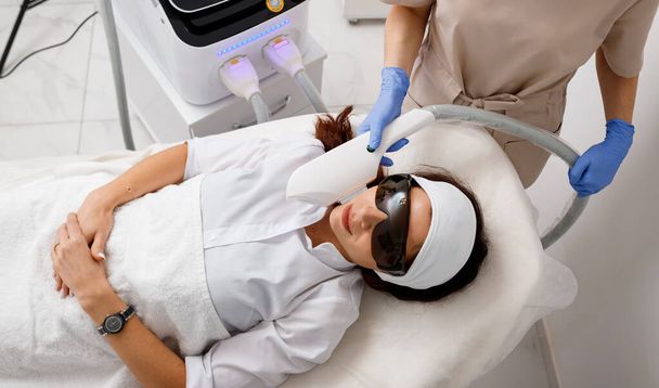 Professional cosmetologist is making cavitation rejuvenation skin treatment in clinic. Radio wave lifting. Beautician hand holding ultrasound device for face lifting procedure - Photo, image
