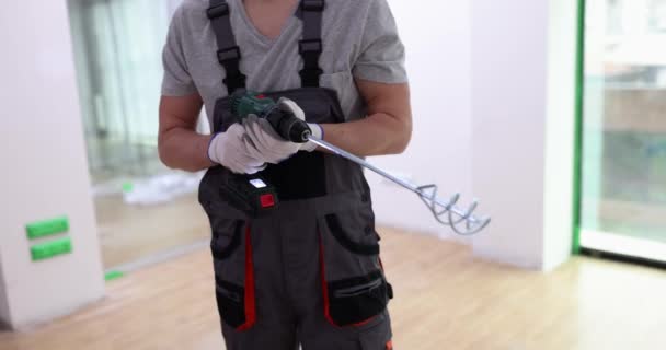 Mężczyzna w mundurze trzyma sprzęt do mieszania farby, zbliżenie. Przygotowanie do malowania mieszkania, naprawa - Materiał filmowy, wideo