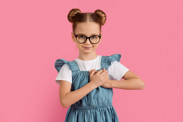 Gratitude Concept. Portrait of cute little girl keeping hands on chest and looking at camera, smiling preteen female child expressing appreciation, standing over pink studio background, copy space - Фото, изображение