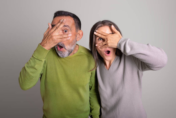 Shocked frightened old european man and woman with open mouth covers eyes with hands on gray studio background, ad and offer. Fear, scare, people emotions and facial expression - Photo, Image