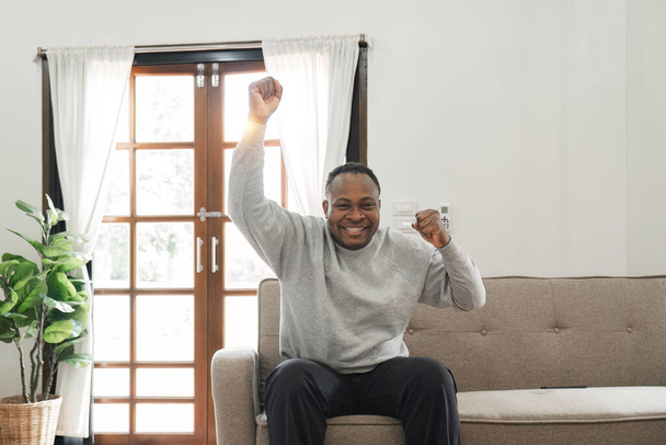 Homem americano africano feliz se divertindo em casa, gritando com controle remoto em sua mão, assistindo jogo de futebol na TV, espaço vazio. preto cara aproveitando seu fim de semana, assistindo TV no sala de estar.. - Foto, Imagem