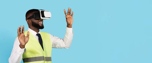 Amazed Black Male Construction Engineer Wearing VR Glasses Over Blue Background, Excited African American Builder Man Enjoying Virtual Reality Experience And Modern Technologies, Copy Space - Foto, Bild