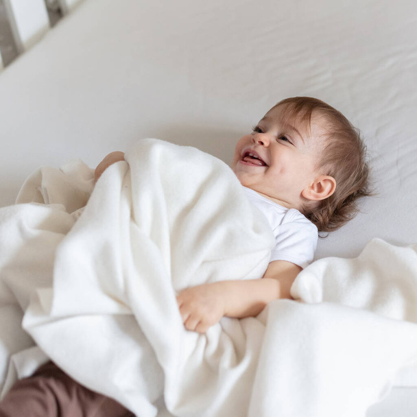 Suloinen 12 kuukauden ikäinen lapsi sängyssä leikkii huopalla - Valokuva, kuva