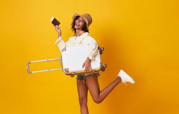 Happy woman traveler standing and holding suitcase with passport isolated on yellow background, Tourist girl having cheerful holiday trip concept, - Photo, Image