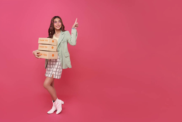 Glücklich asiatische Frau lächelnd mit Paketkasten zeigt mit dem Finger isoliert auf rosa Kopierraum Hintergrund. - Foto, Bild