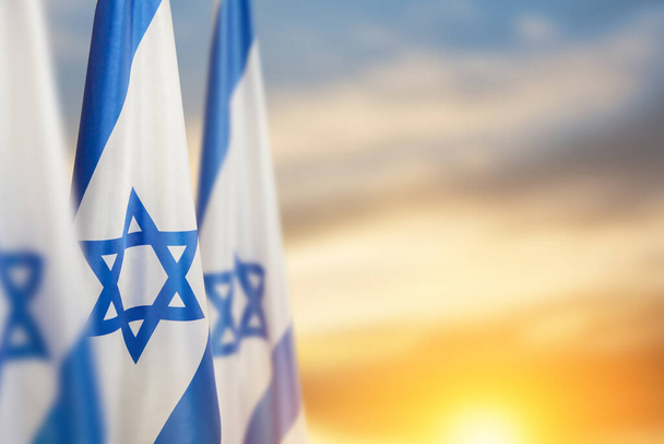 Israel flags with a star of David over cloudy sky background on sunset. Patriotic concept about Israel with national state symbols. Banner with place for text. - Фото, зображення