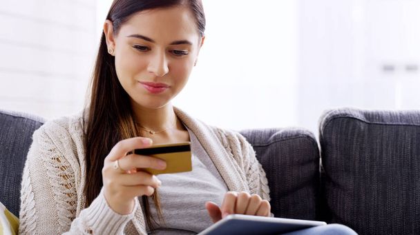 Doing some shopping in the comfort of my own home. an attractive young woman using her credit card and digital tablet while relaxing on a sofa at home - Foto, immagini